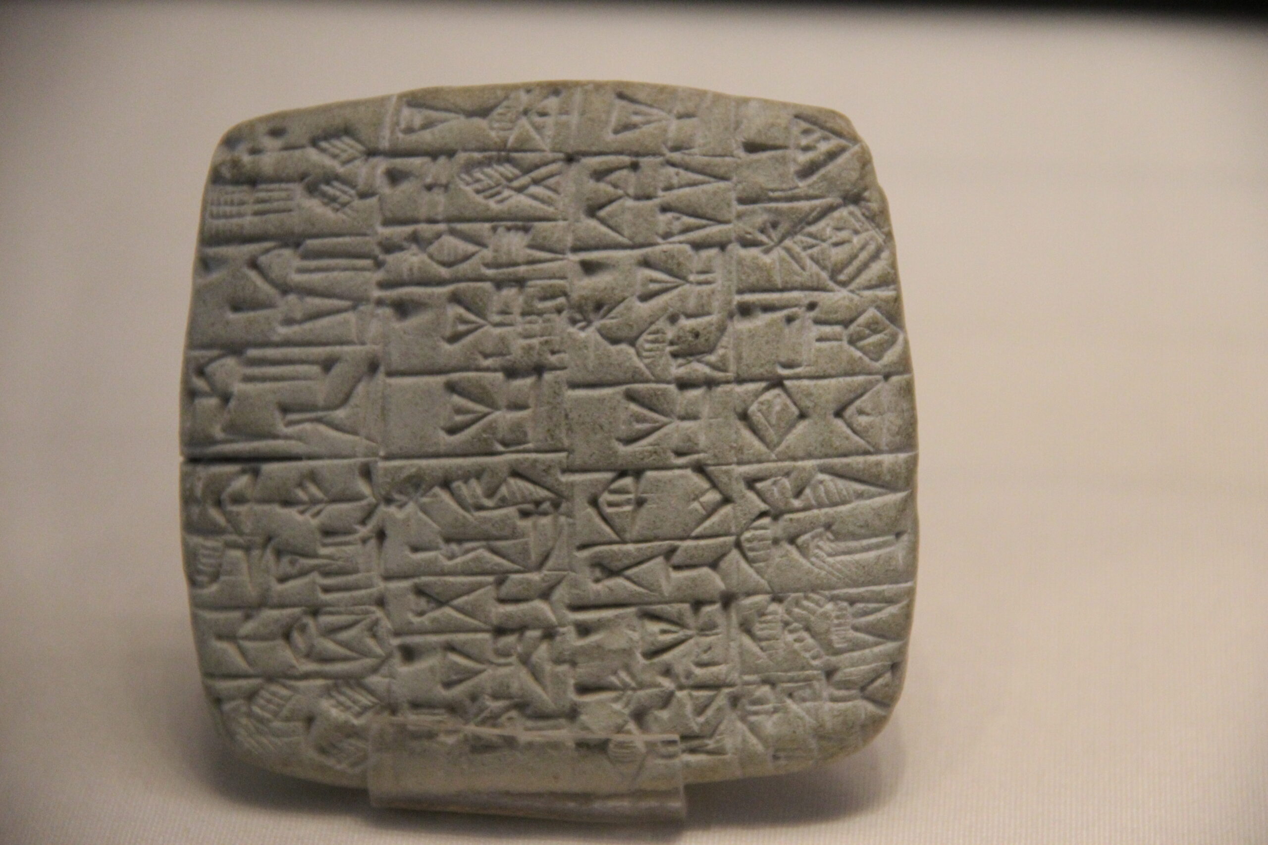 Tablilla sumeria de arcilla con escritura cuneiforme, iluminación dramática sobre fondo oscuro